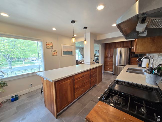 Kitchen featuring brown cabinets, a sink, light countertops, freestanding refrigerator, and range hood | Image 18
