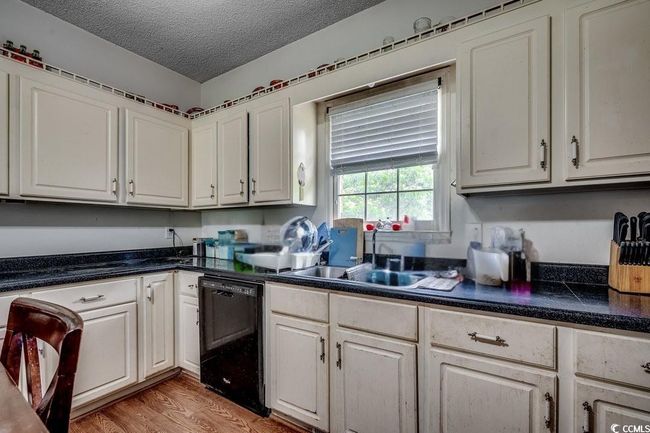 Kitchen featuring black dishwasher, a sink, a textured ceiling, dark countertops, and white cabinets | Image 14