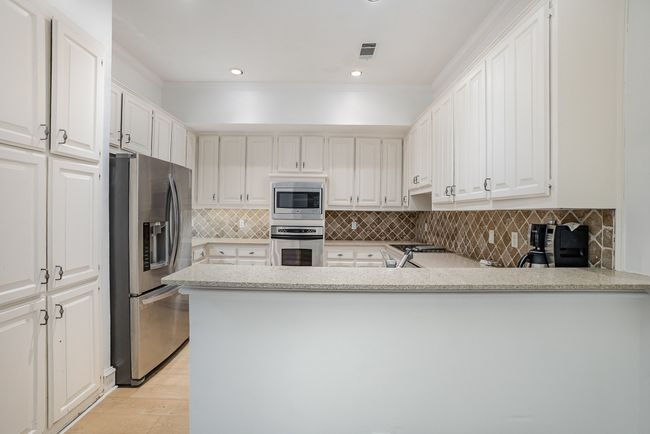 Kitchen with visible vents, white cabinets, appliances with stainless steel finishes, a peninsula, and light wood-style floors | Image 9