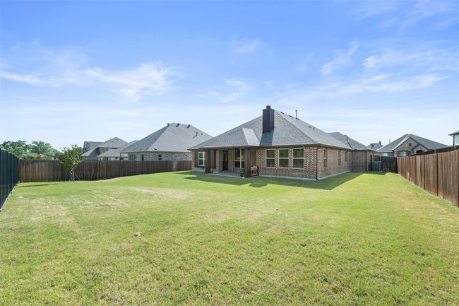 Rear view of property featuring brick siding, a fenced backyard, a chimney, and roof with shingles | Image 35