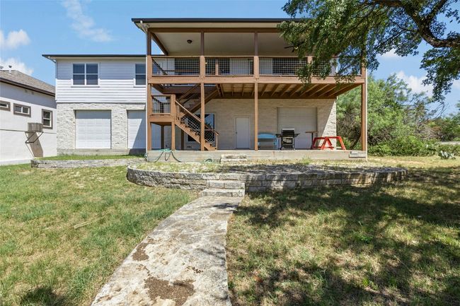Rear view of property featuring an attached garage door that opens to large unfinished area, a deck, stairway, a yard, and a patio area | Image 28