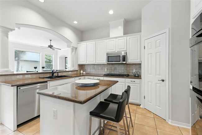 Kitchen with stainless steel appliances, a kitchen island, arched walkways, white cabinets, and backsplash | Image 14