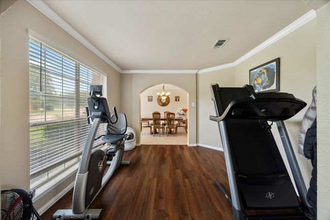 Exercise room with arched walkways, dark wood finished floors, crown molding, baseboards, and a chandelier | Image 9
