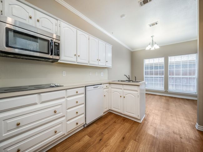 Kitchen with stainless steel microwave, dishwasher, light wood-style flooring, a peninsula, and a chandelier | Image 11