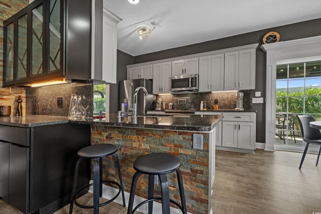 Kitchen featuring stainless steel appliances, a peninsula, glass insert cabinets, a breakfast bar, and dark stone countertops | Image 13