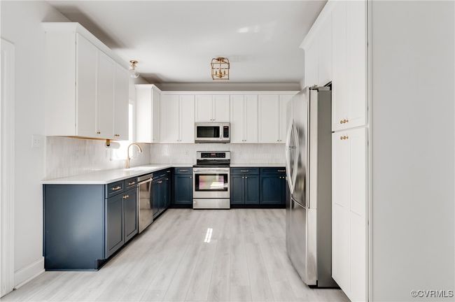 Kitchen with appliances with stainless steel finishes, blue cabinetry, light wood-style flooring, backsplash, and white cabinets | Image 13