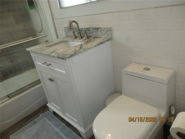Full bathroom featuring bath / shower combo with glass door, vanity, tile walls, and toilet | Image 14