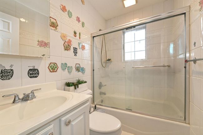 Full bath with tile walls, toilet, shower / bath combination with glass door, and vanity | Image 8