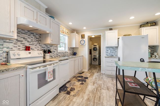 kitchen with white appliances, under cabinet range hood, stacked washer / drying machine, crown molding, and tasteful backsplash | Image 14