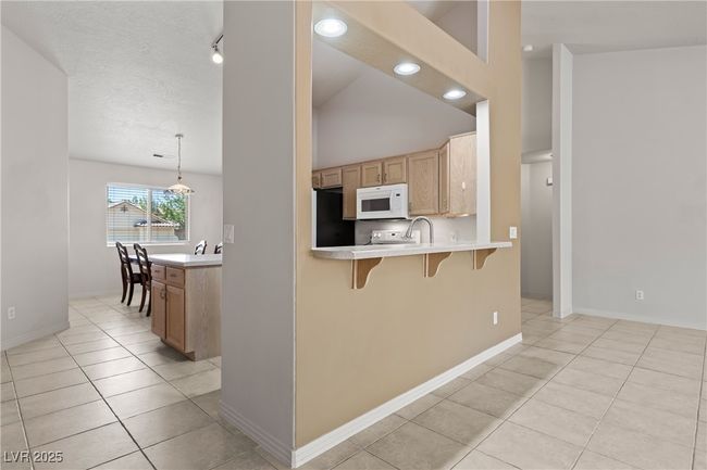 Kitchen with white microwave, a kitchen breakfast bar, light tile patterned floors, light countertops, and recessed lighting | Image 13