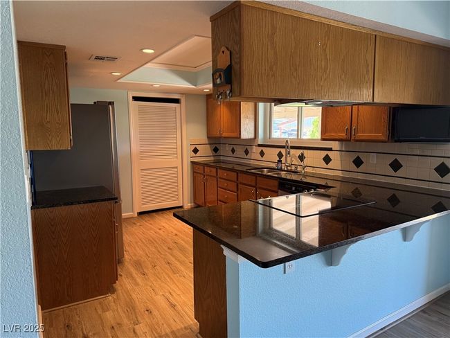 Kitchen with a sink, light wood-style floors, a peninsula, decorative backsplash, and brown cabinets | Image 11