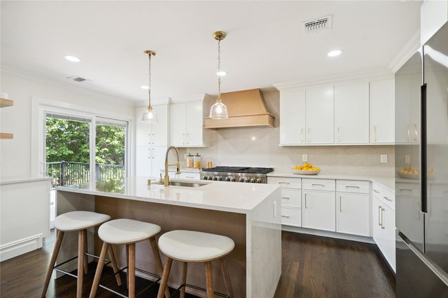 Kitchen featuring fridge, custom range hood, dark wood finished floors, light countertops, and tasteful backsplash | Image 9