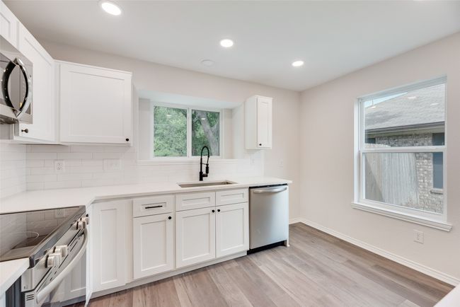 Kitchen with stainless steel appliances, a sink, decorative backsplash, white cabinets, and light countertops | Image 9