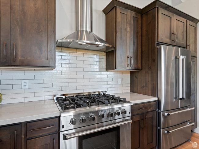 Kitchen featuring premium appliances, wall chimney range hood, and dark brown cabinets | Image 19