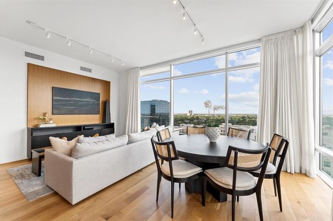 This modern living space features large windows with stunning city views, a comfortable seating area, and a dining table with elegant chairs. The room is bright and airy, enhanced by light floors and minimalist decor. | Image 8