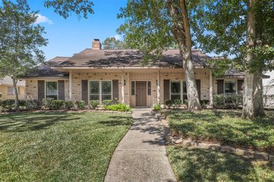 This is a charming single-story home featuring a brick exterior, inviting front porch, and mature shade trees, located on a well-manicured lawn. | Image 1