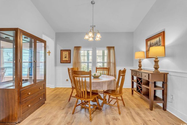 Dining space with light wood-style floors, a notable chandelier, lofted ceiling, and a wainscoted wall | Image 15