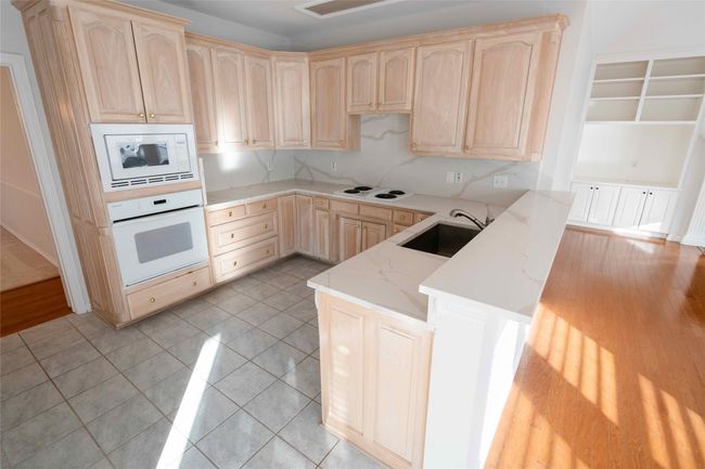 Kitchen with white appliances, light brown cabinetry, light stone countertops, and light tile patterned flooring | Image 15