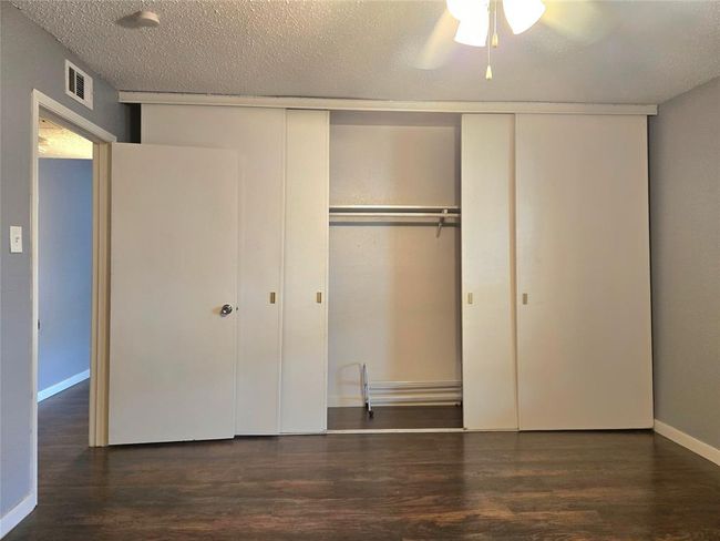 This room features a spacious closet with sliding doors, hardwood flooring, and a ceiling fan, offering a clean and functional space. | Image 8