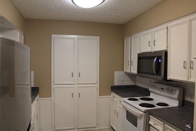 Kitchen featuring stainless steel microwave, white electric range oven, dark countertops, white cabinetry, and wainscoting | Image 6