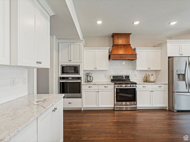 Kitchen featuring appliances with stainless steel finishes, custom range hood, decorative backsplash, white cabinets, and recessed lighting | Image 11