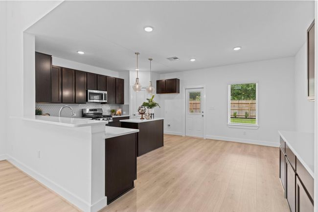 The kitchen opens beautifully into the main living space, showcasing a modern layout with wood-like vinyl plank flooring, pendant lighting, and ample counter space for both meal prep and casual gatherings. **Image Representative of Plan Only and May Vary as Built**. | Image 9