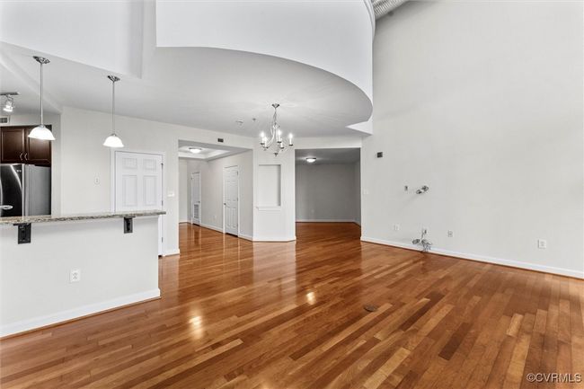 Unfurnished living room featuring baseboards, a notable chandelier, a towering ceiling, and light wood-style flooring | Image 14