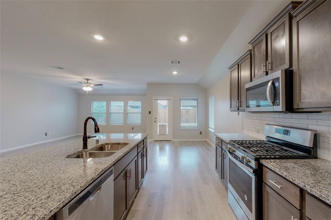 Kitchen featuring light stone counters, decorative backsplash, a sink, stainless steel appliances, and dark brown cabinetry | Image 16