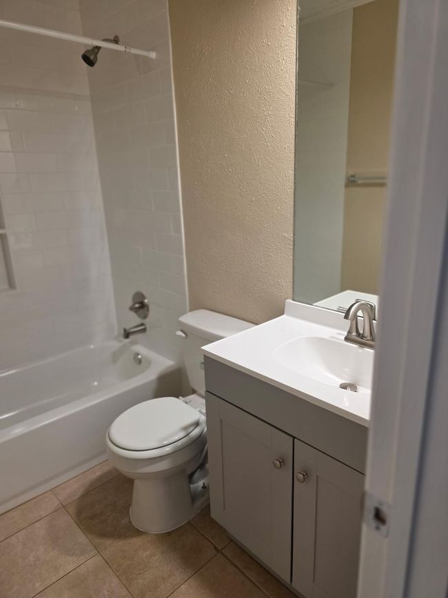 Full bathroom with a textured wall, bathtub / shower combination, vanity, and tile patterned flooring | Image 9