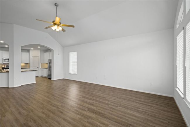 Unfurnished living room featuring lofted ceiling, ceiling fan, arched walkways, baseboards, and dark wood-style floors | Image 7