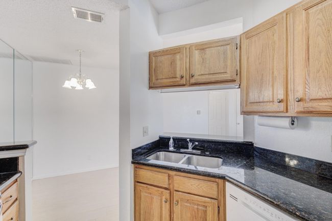 Kitchen featuring a sink, dishwasher, a chandelier, dark stone countertops, and decorative light fixtures | Image 7