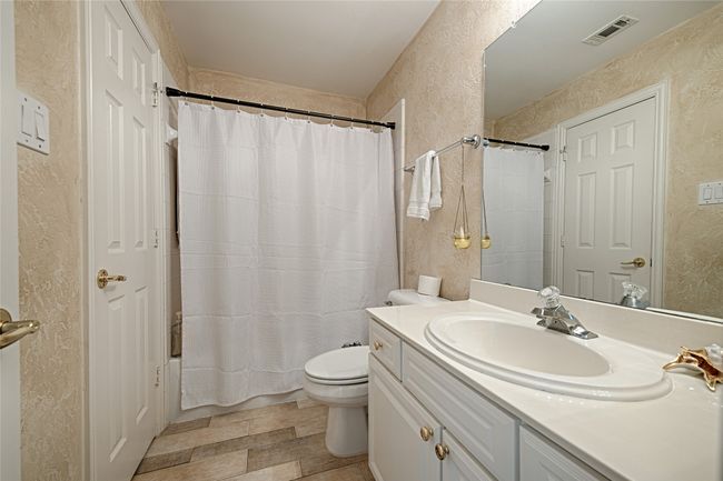 Full bathroom with a textured wall, toilet, vanity, visible vents, and shower / bath combo with shower curtain | Image 11