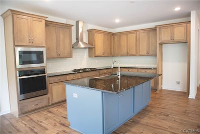 Kitchen with tasteful backsplash, light wood-type flooring, an island with sink, wall chimney exhaust hood, and appliances with stainless steel chef's kitchen | Image 3