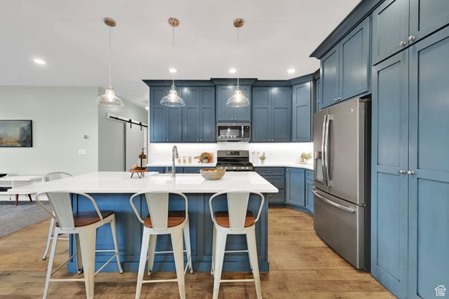 Kitchen with stainless steel appliances, a barn door, a breakfast bar, light wood-type flooring, and recessed lighting | Image 11