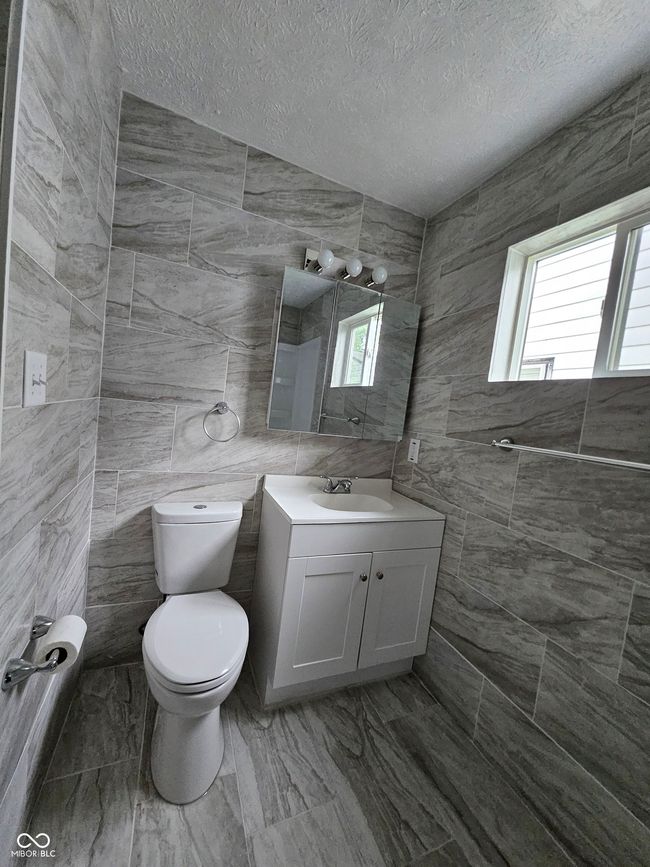 bathroom with tile walls, toilet, vanity, healthy amount of natural light, and a textured ceiling | Image 7