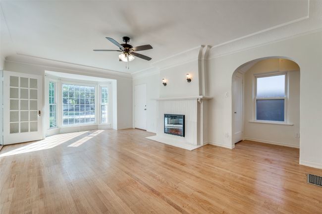 Unfurnished living room featuring ceiling fan, ornamental molding, a fireplace with flush hearth, arched walkways, and light wood-style floors | Image 5