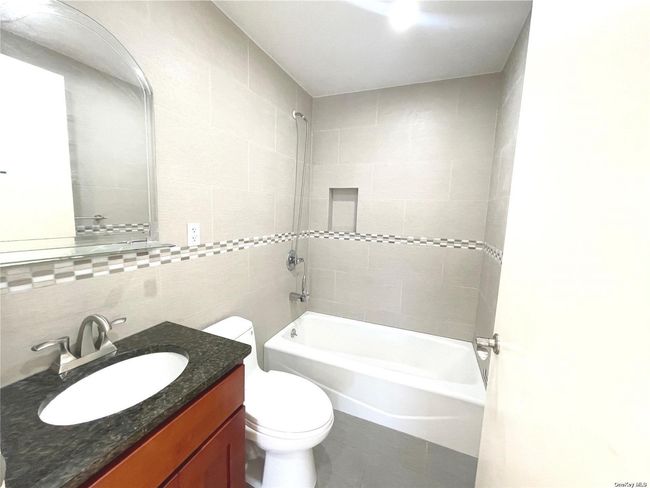 Full bathroom with vanity, tile patterned flooring, tiled shower / bath combo, toilet, and tile walls | Image 9