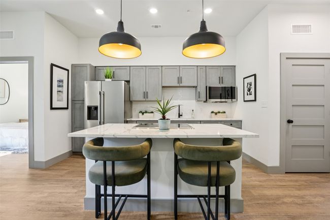 Kitchen with backsplash, light wood-style floors, decorative light fixtures, a breakfast bar, and light stone counters | Image 6