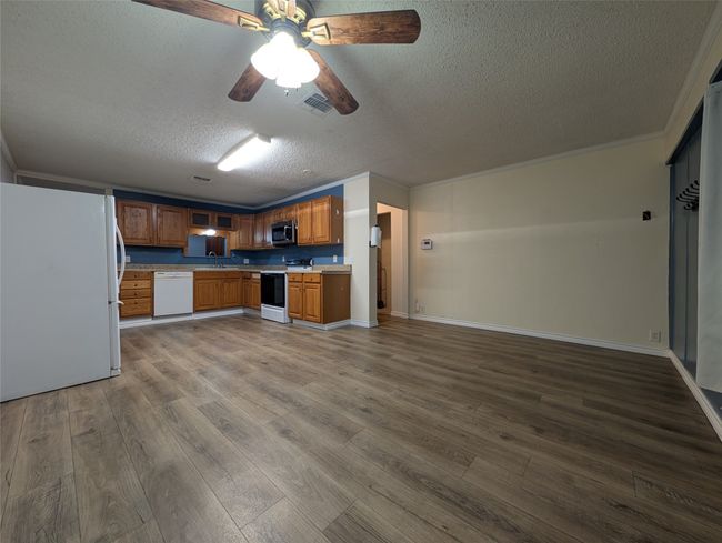 Kitchen with a textured ceiling, visible vents, white appliances, light countertops, and dark wood-type flooring | Image 4