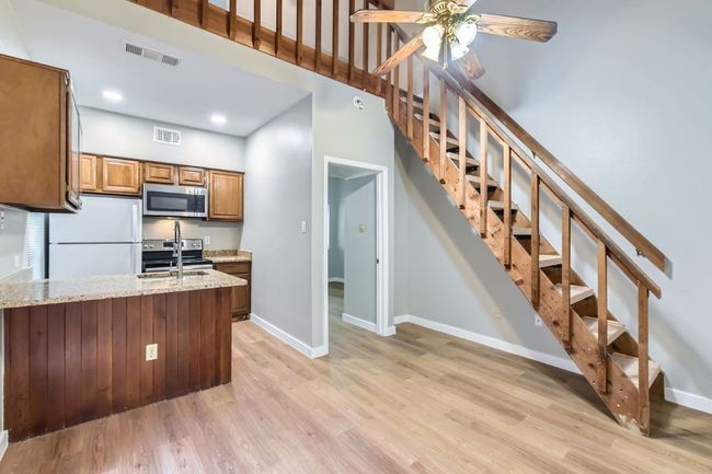 Kitchen featuring visible vents, brown cabinets, light wood-type flooring, a sink, and appliances with stainless steel finishes | Image 4