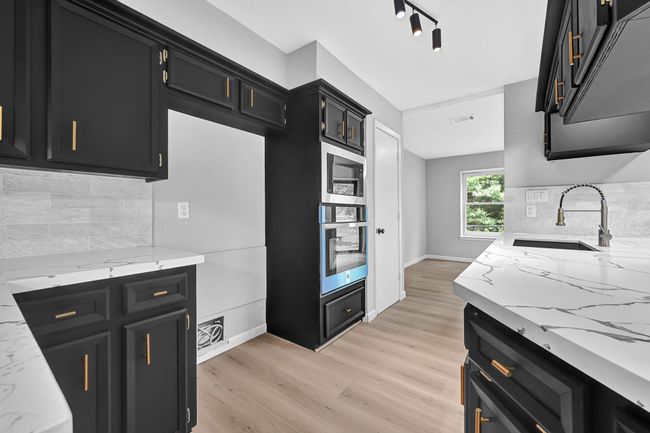Another stunning angle of the fully updated kitchen showcasing brand-new stainless steel double ovens, dramatic quartz countertops, modern backsplash tile, and matte black cabinetry with sleek gold hardware. The open layout and natural light create a bright, functional space perfect for entertaining. | Image 16