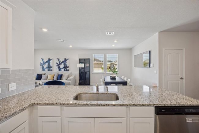 Kitchen featuring stainless steel dishwasher, white cabinets, open floor plan, light stone countertops, and recessed lighting | Image 22