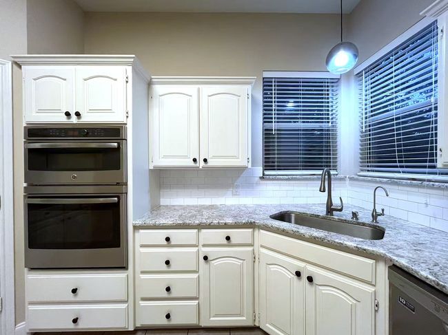 Kitchen featuring dishwashing machine, double oven, tasteful backsplash, light stone countertops, and decorative light fixtures | Image 8