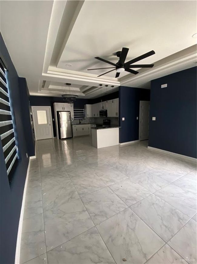 Unfurnished living room featuring a ceiling fan, light marble finish floors, and a tray ceiling | Image 4