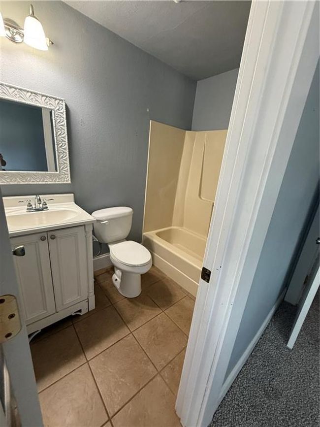 Bathroom with toilet, vanity, tile patterned floors, washtub / shower combination, and baseboards | Image 24