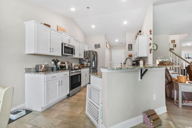 Kitchen with stainless steel appliances, lofted ceiling, light stone countertops, white cabinets, and a peninsula | Image 11
