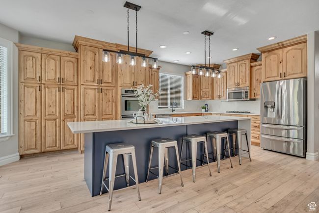 Kitchen with stainless steel appliances, a kitchen island, light countertops, a breakfast bar, and light wood-type flooring | Image 10