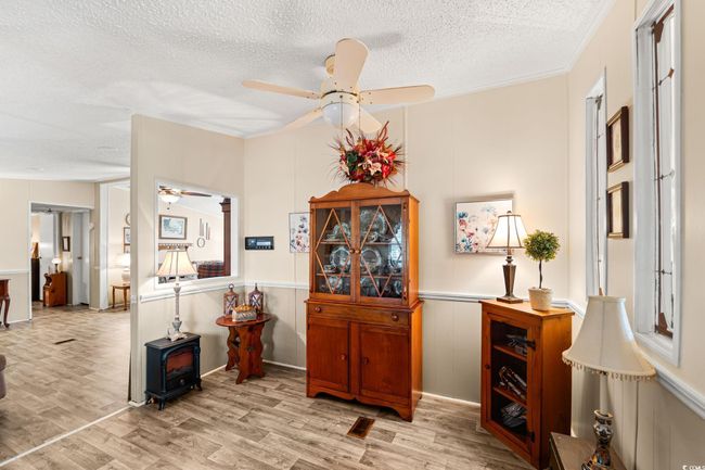 Dining room with a ceiling fan, a wood stove, a textured ceiling, light wood-type flooring, and a decorative wall | Image 18