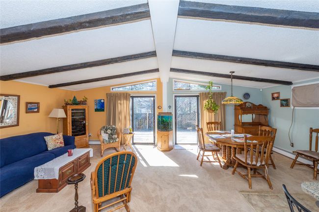 Living area with a textured ceiling, vaulted ceiling with beams, a baseboard radiator, light carpet, and baseboards | Image 5
