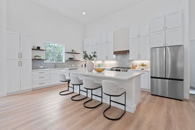 Kitchen featuring open shelves, a breakfast bar area, stainless steel fridge, a center island, and light quartz countertops | Image 11